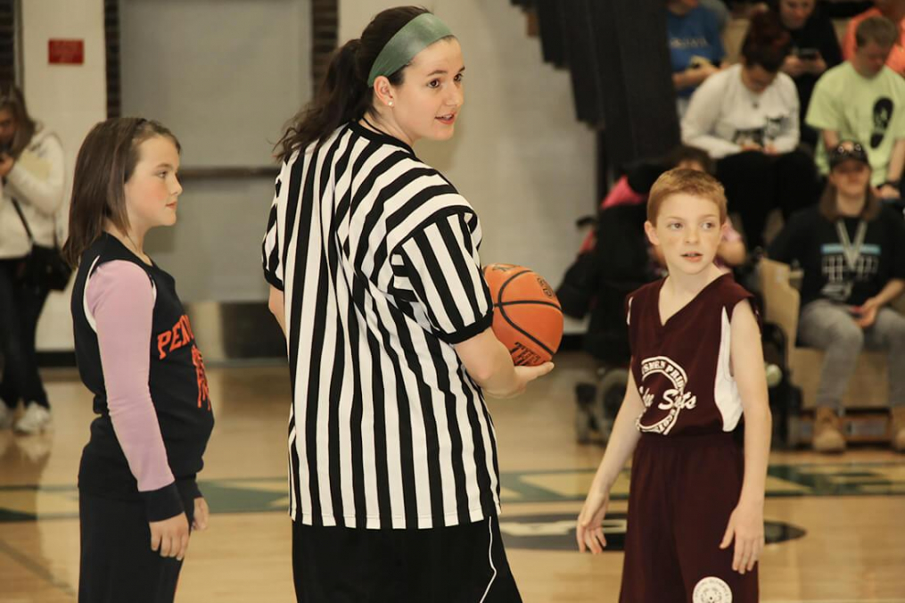 A student and community children stand on the David M. Sweet Court in the Recreation and Athletics Center.